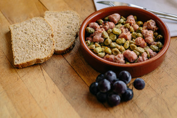 Bean appetizer with onion and sausage presented in a clay plate on a wooden board. Traditional Spanish food. Space for text