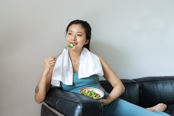 A young Asian woman eating a healthy vegetable salad in the living room