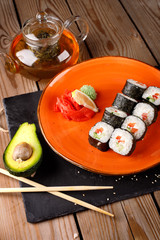 A set of baked sushi rolls with wasabi and ginger on an orange plate background.