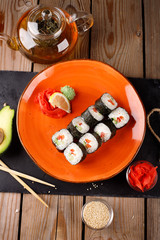 A set of baked sushi rolls with wasabi and ginger on an orange plate background.