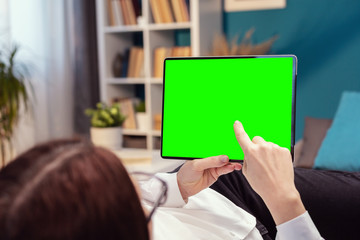 Rear view of person touching tablet with green screen lying on bed or couch in flat