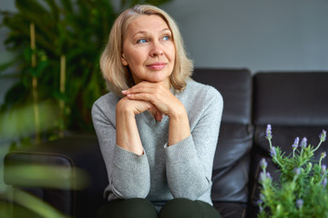 Lovely middle-aged blond woman sitting on a sofa at home.