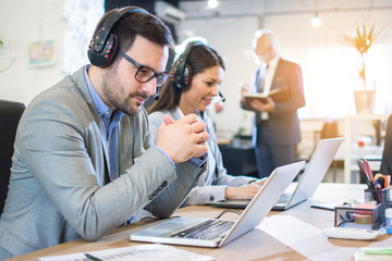 Concentrated business man with hands clasped wearing headset and working on laptop in office