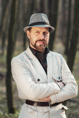 Half-body portrait of confident presentable man with folded arms standing in nature looking at camera