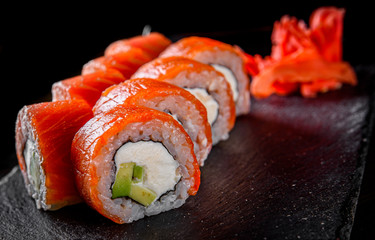 sushi roll with salmon, avocado, cream cheese in plate on black wooden table background
