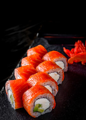 sushi roll with salmon, avocado, cream cheese in plate on black wooden table background