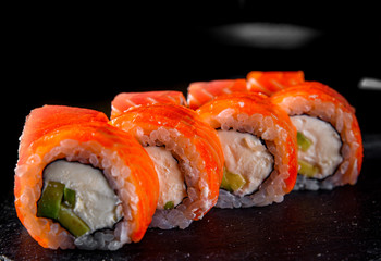 sushi roll with salmon, avocado, cream cheese in plate on black wooden table background