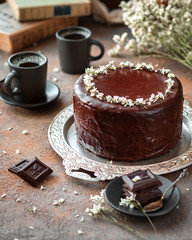 Chocolate cake with chocolate icing, two cups of coffee decorated with flowers on a gray background vertical