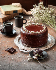 Chocolate cake with chocolate icing, two cups of coffee decorated with flowers on a gray background vertical