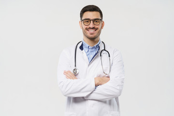 Portrait of smiling young male doctor with stethoscope around neck standing with crossed arms in...