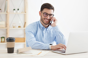 Young business man wearing glasses, working in office, looking attentively at screen, typing,...