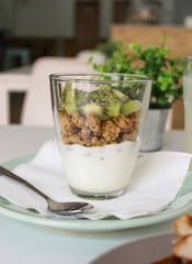 Glass of yogurt with granola and fruit kiwi in a green plate with restaurant background vertical