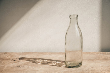 Glass transparent bottle on wooden table on white wall background. Copy, empty space for text