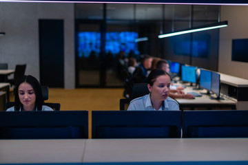Group of Security data center operators (administrators) working in a group at a CCTV monitoring room while looking at multiple monitors ( computer screens)
