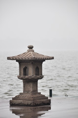 Obraz na płótnie Canvas A traditional Chinese stone lantern stands on the edge of West Lake in Hangzhou. The background is blurry in the fog.