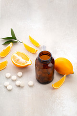 Vitamins lying near dark glass jar  with lemon slice and whole fruit on white wooden table 
