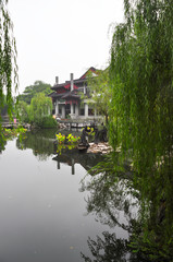 Obraz premium A Chinese building on the shores of West Lake in Hangzhou. The trees and the house are reflected in the water.