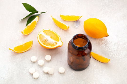 Vitamins lying near dark glass jar  with lemon slice and whole fruit on white wooden table 
