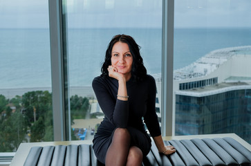 Elegant brunette woman inside apartament. Lady in dark grey dress. Woman sitting on sofa, panoramic...