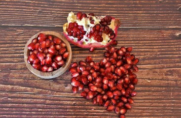 red pomegranate seeds in a wooden bowl and on a wooden table