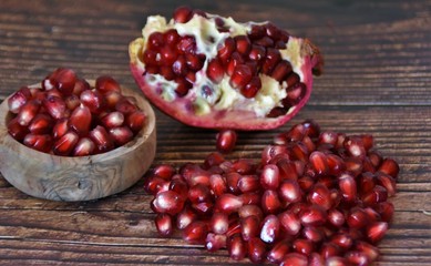 red pomegranate seeds in a wooden bowl and on a wooden table