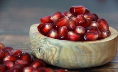 red pomegranate seeds in a wooden bowl and on a wooden table