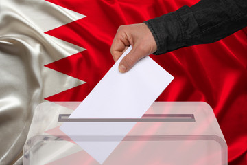 male voter drops a ballot in a transparent ballot box against the backdrop of the Bahrain national flag, concept of state elections, referendum
