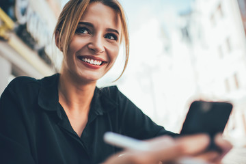 Cheerful Caucasian woman with candid smile on face feeling happiness during smartphone networking...