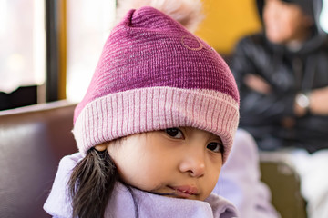 Pretty female child wearing purple coat and cute bonnet while sitting inside a bus and sleepy, Her lips are dry because of the cold weather