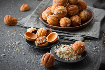 homemade cookies in the form of nuts with a filling boiled condensed milk stacked in a pyramid in a wooden plate on a gray background