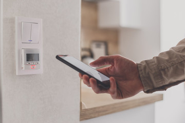 Smartphone connecting to floor heating controller in kitchen. Remote home control system on a smartphone.