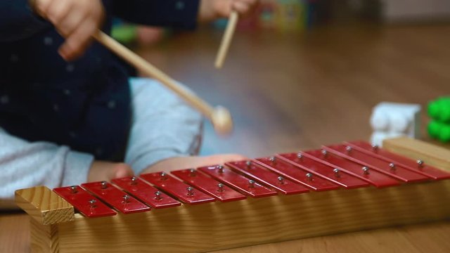 The child plays with sticks on the red xylophone, percussion instrument, close up