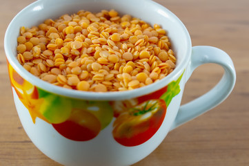 Tasty pumpkin cream soup served with croutons in light yellow mug on matching napkin. Carved pumpkin piece, red lentils and meant leaves are around on light gray background.