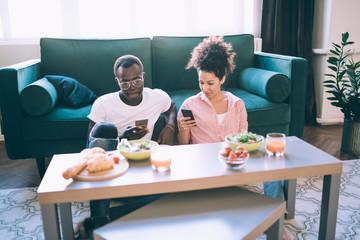 Fototapeta na wymiar Multiethnic couple using smartphones during dinner at home