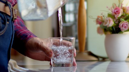 Man pouring water from a clear jug into a water glass