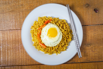 fried noodles or mie goreng with fried egg or telur mata sapi on the top. has a savory taste. in white plate on wooden background. top view food