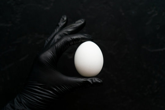 A woman's hand in a black glove holds a white egg ready to paint it