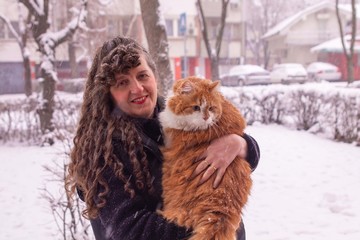 Woman with curly hair smiling and holding an orange furry cat in a snowy day