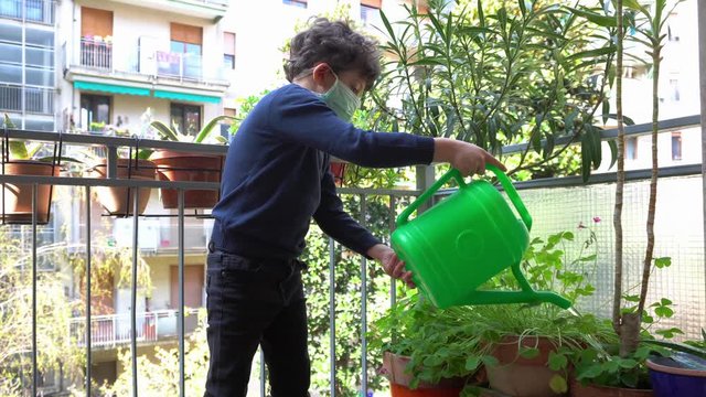 Europe, Italy , Milan - children boy  five yewith mask ars at home during quarantine due n-cov19 Coronavirus outbreak - life stile in apartment - water the plant and flowers on the balcony