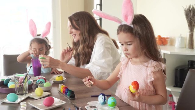 happy family preparing for easter. mother with daughters with funny bunny ears painting easter eggs together, 4K.