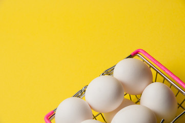 Chicken eggs in a metal grocery basket on a yellow background