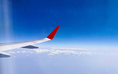 Wing of an airplane flying above in the morning with blue sky and clouds background.