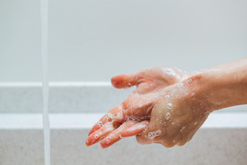 Fototapeta premium Close-up of woman rubbing hands with a soap under bathroom sink.