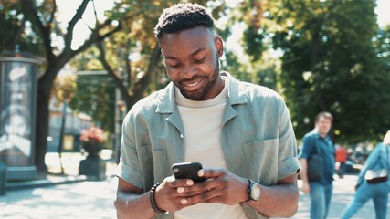 attractive african american young man walks down the street uses phone smile sunlight sunset cellphone fashion internet face outside technology black city mobile summer happy