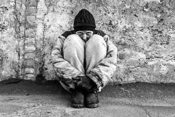 Dirty homeless woman sits under a gray wall