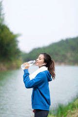A young Asian woman drinks water by the lake