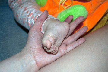 Little baby foot in a female palm. At home
