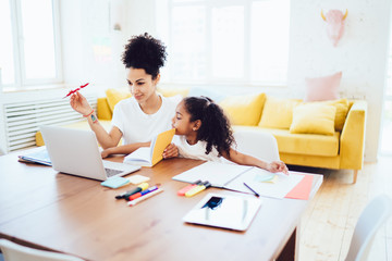 Mother using laptop with little curious daughter near