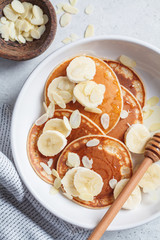 Traditional pancakes with banana, almonds and honey in white plate, top view.