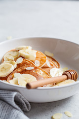 Traditional pancakes with banana, almonds and honey in white plate.
